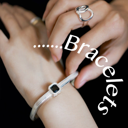 A hand with silver rings adjusts a silver bracelet with black gemstone. Original design bracelets.